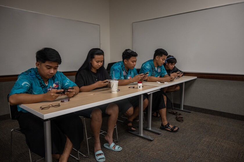 Cinco alunos estão jogando um jogo para celular em seus telefones.
