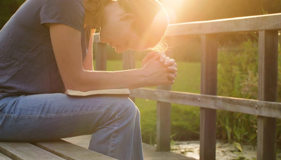 mulher com a Biblia no colo, de cabeça baixa buscando revelação