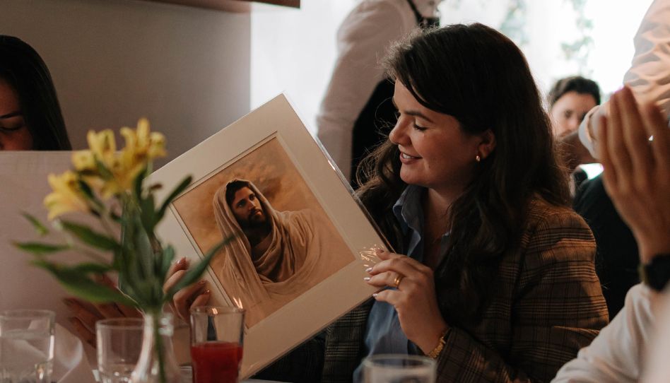 Uma mulher em uma mesa de jantar observando uma pintura de Jesus Cristo.